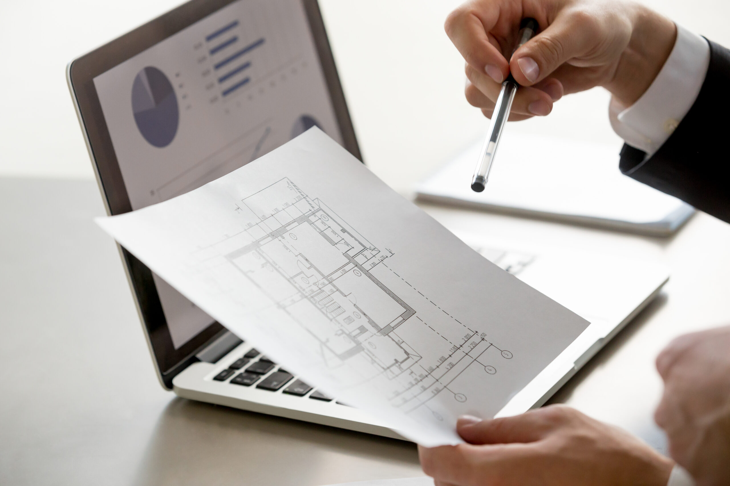 male hand holding project plan, statistics on screen, close up